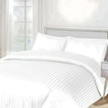 White striped bedding set on a bed with a neutral headboard.