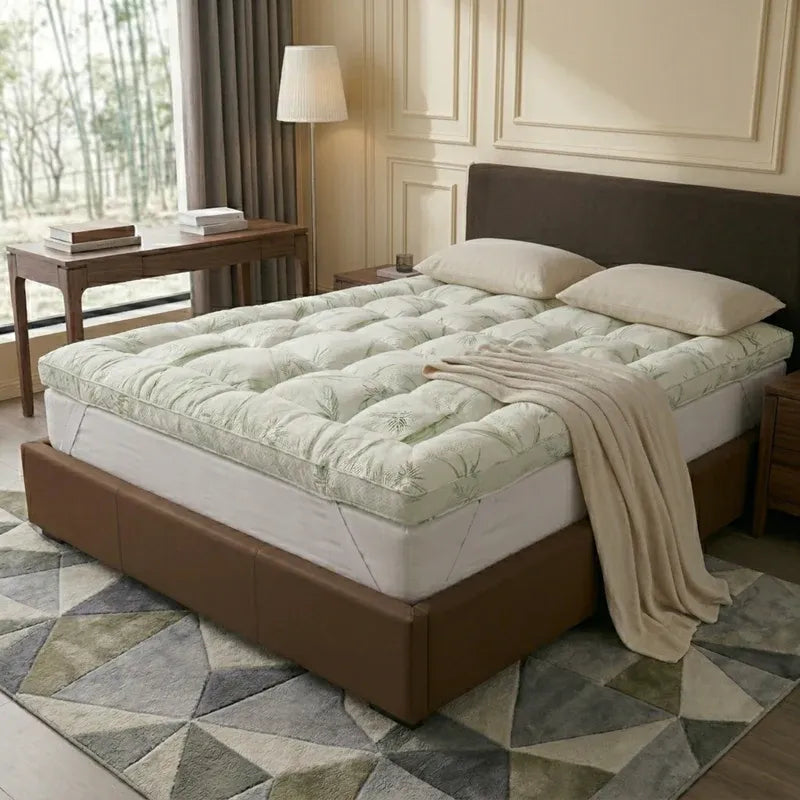 Mattress topper on a bed in a bedroom setting with a lamp and table.