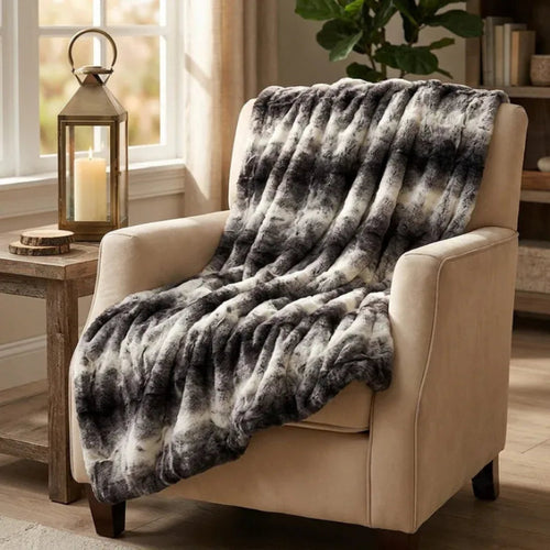Beige armchair with a gray and white patterned throw blanket, next to a wooden side table with a candle and lantern.