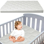 Baby sitting on a crib mattress with a white crib in the background