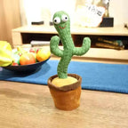 Plush cactus toy on a wooden table with a bowl of fruit in the background