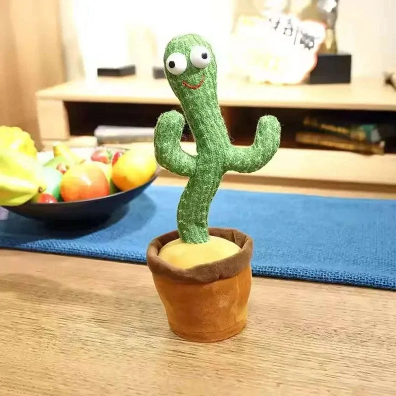 Plush cactus toy on a wooden table with a bowl of fruit in the background