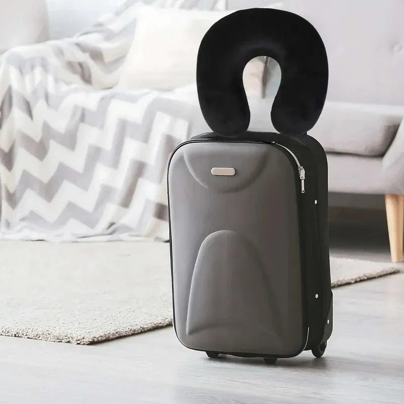 Gray suitcase with a black neck pillow on a light wooden floor.