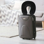 Gray suitcase with a black neck pillow on a light wooden floor.