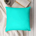 Turquoise pillow on a wooden surface with a book and bottle in the background