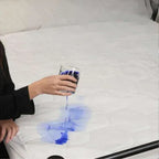 Person pouring blue liquid from a glass onto a white surface, creating an abstract pattern.