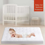 Baby lying on a mattress protector with a crib in the background