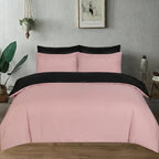 A bed dressed in a pink and black bedding set, featuring a pink duvet cover and matching pillowcases with solid black top borders, styled in a bedroom setting with a plant, wall art, and side table.