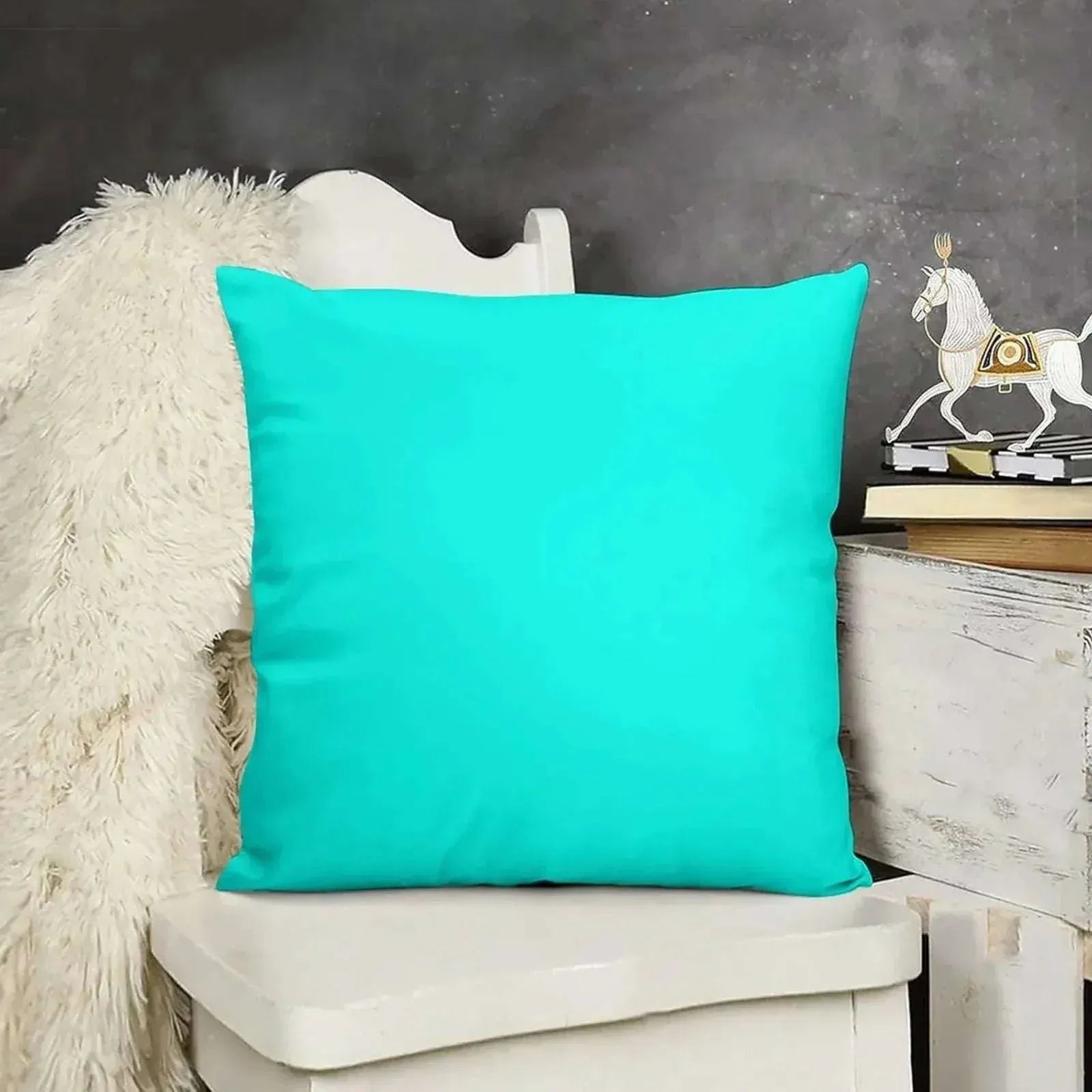 Turquoise pillow on a white chair with a decorative horse figure in the background.