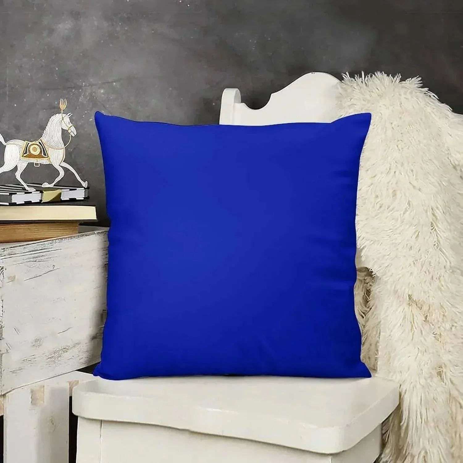 Blue pillow on a white chair with a gray wall and decorative items in the background