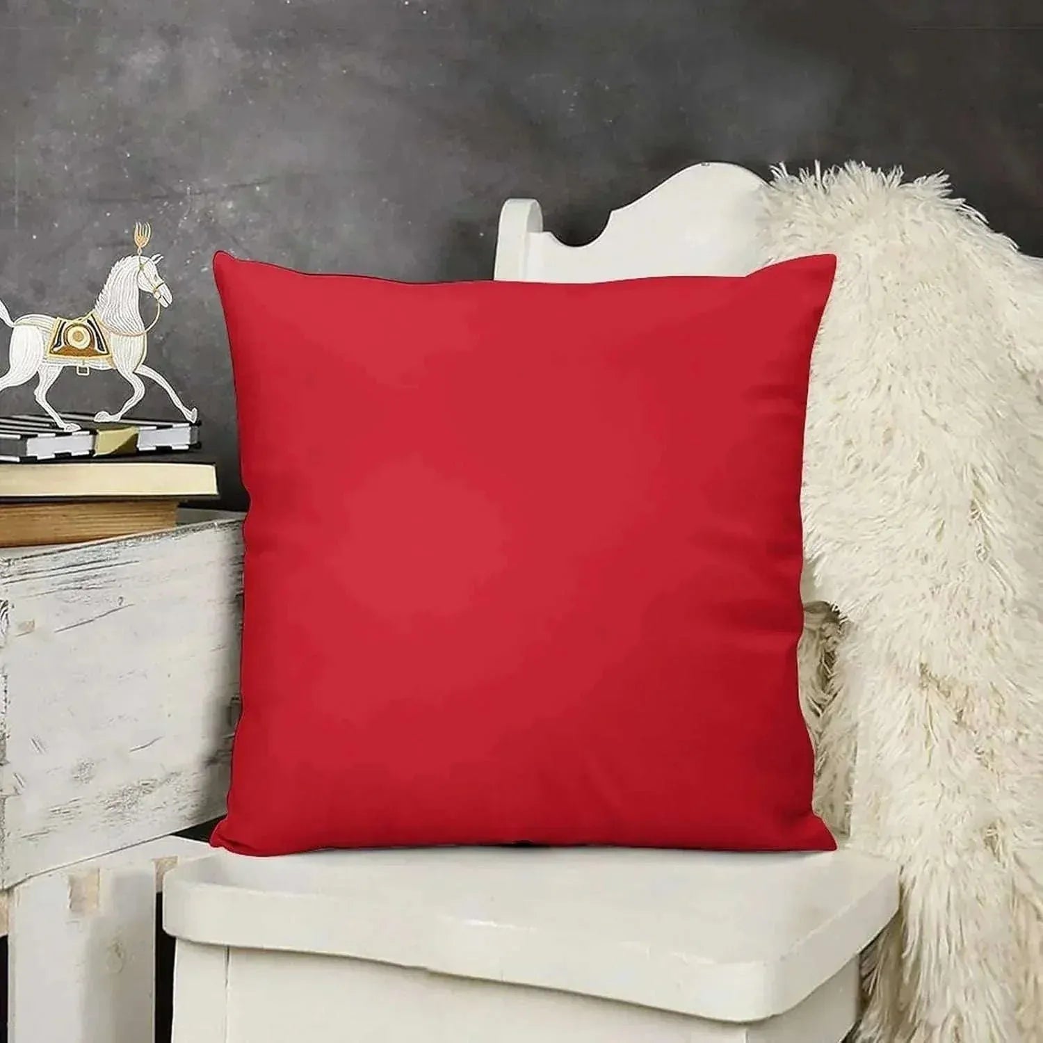 Red pillow on a white chair with a dark gray wall and decorative items in the background
