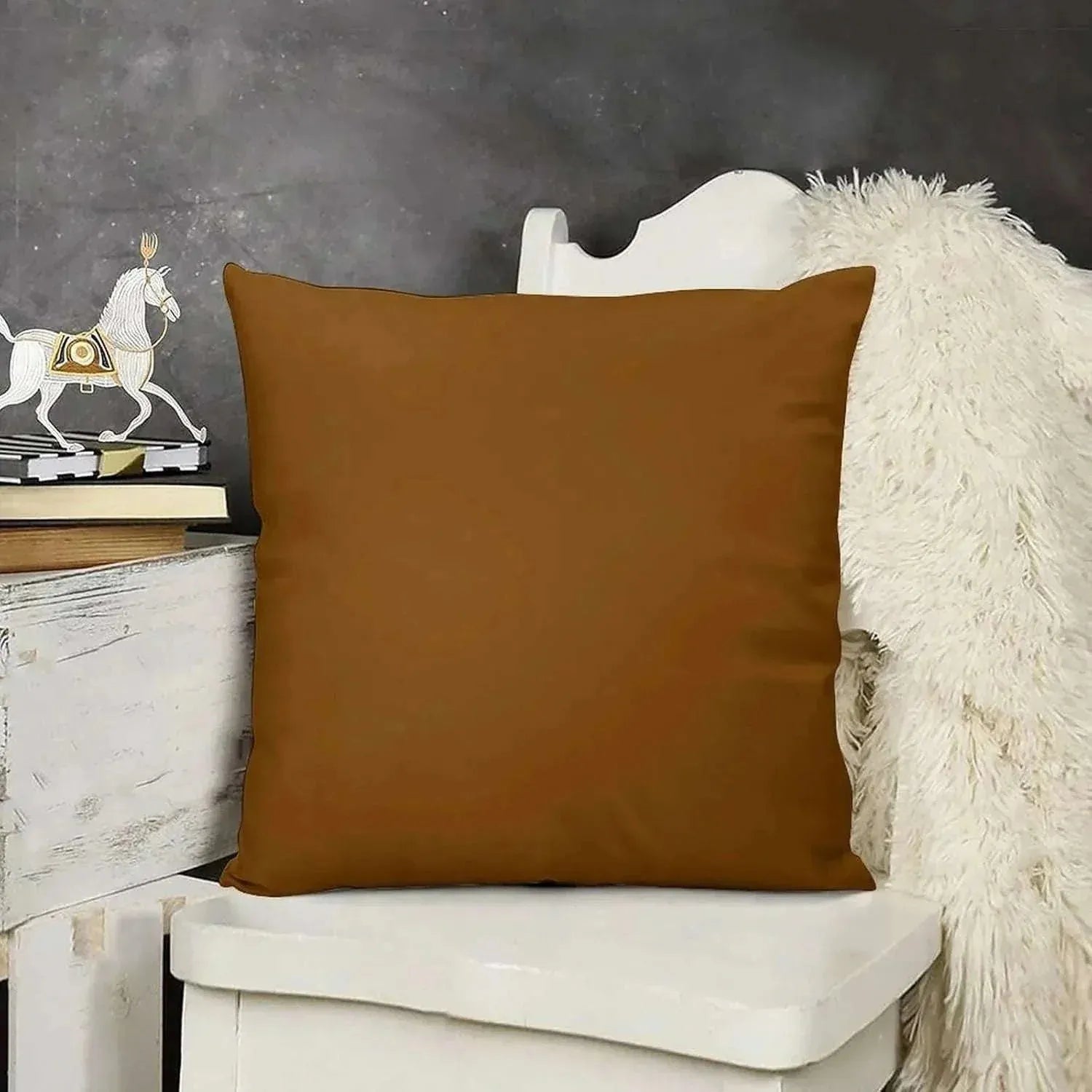 Brown pillow on a white chair with a dark gray wall and decorative items in the background
