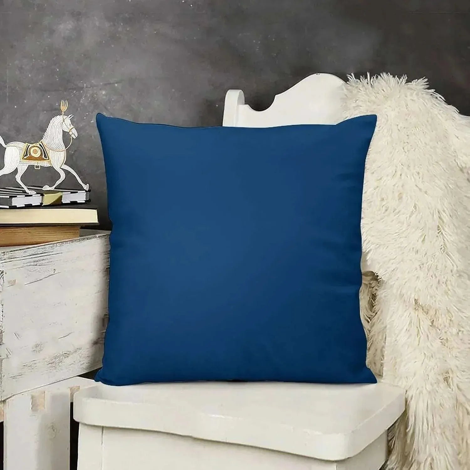 Blue pillow on a white chair with a dark gray wall and decorative items in the background