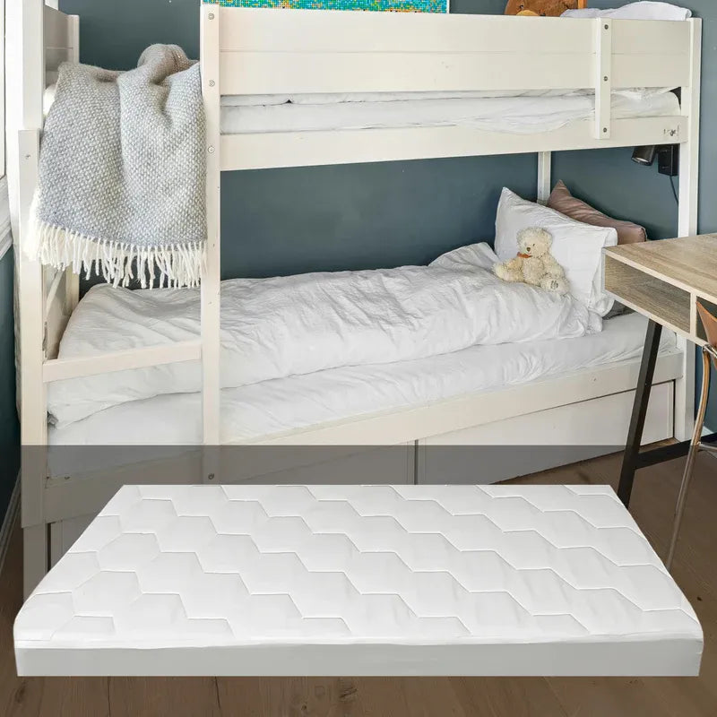 A white quilted mattress topper with a geometric hexagonal pattern, shown floating in front of a light wood bunk bed in a bedroom setting.