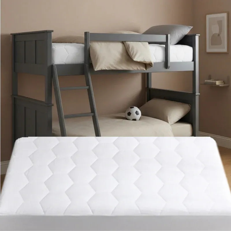 A white quilted mattress shown in the foreground, with a dark gray wooden bunk bed in the background containing beige bedding and a soccer ball.