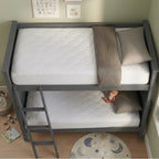 A gray wooden twin-over-twin bunk bed with a ladder, shown with two white mattresses, beige pillows, and a folded beige blanket in a child's bedroom.