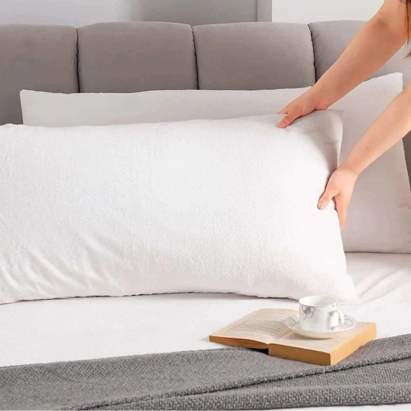 Person adjusting a white pillow on a bed with a gray headboard.